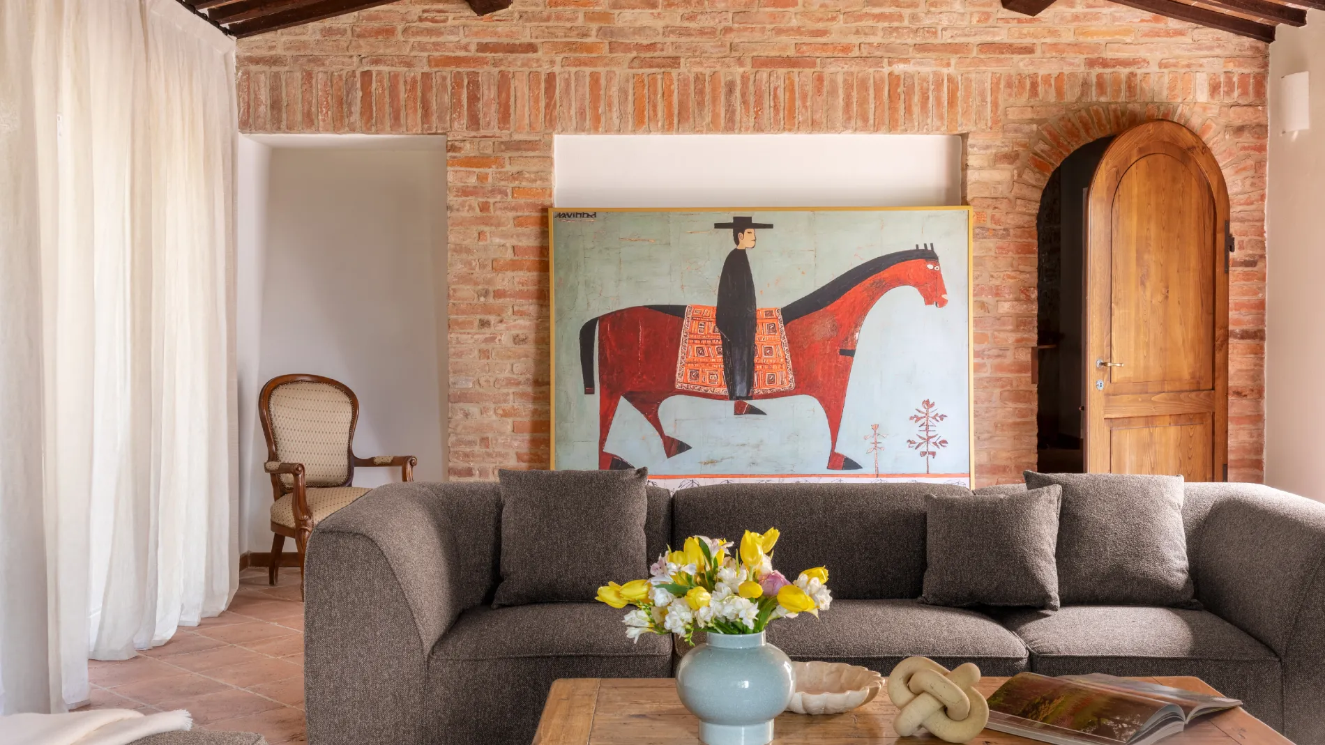 Living room with brick wall, grey sofa and equestrian painting - Villa San Bartolomeo, BZAR hotels in Tuscany